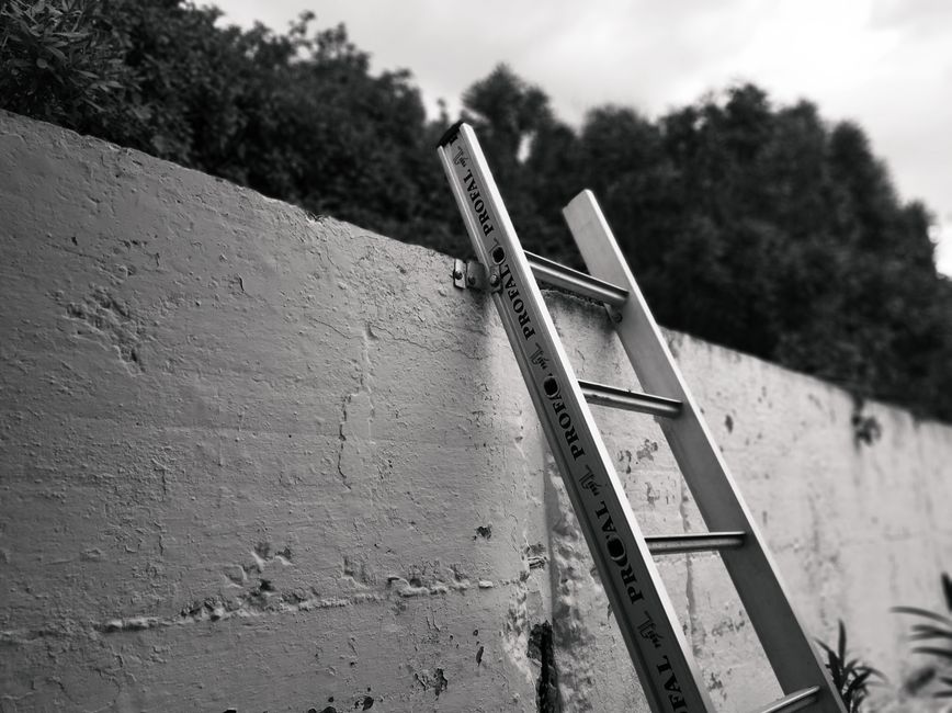 Construction worker using ladder and safety equipment on residential roofing project, demonstrating proper equipment setup and use during rental work